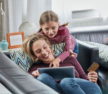 Une mère et sa fille font une commande en ligne sur un ordinateur portable assises sur le canapé