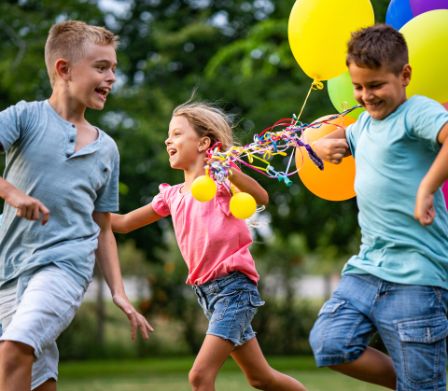 Kinder laufen mit Ballons über die Wiese