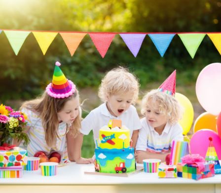 Trois jeunes enfants attablés à une table d’anniversaire à la décoration colorée 