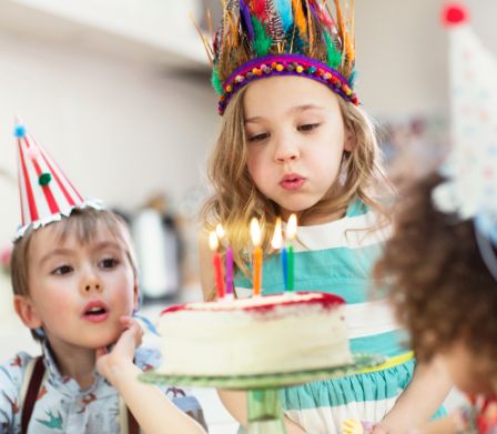 Drei Kinder mit Hütchen und Indianer Kopfschmuck vor Geburtstagskuchen