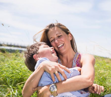 Seduta su un prato, una madre che ride tiene tra le braccia il suo figlioletto