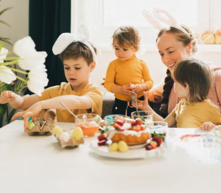 Madre con tre bambini piccoli intorno al tavolo dipingono le uova di Pasqua