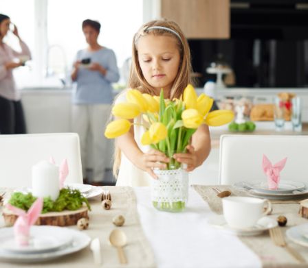 Una bambina poggia dei tulipani freschi su una tavola decorata con motivi pasquali