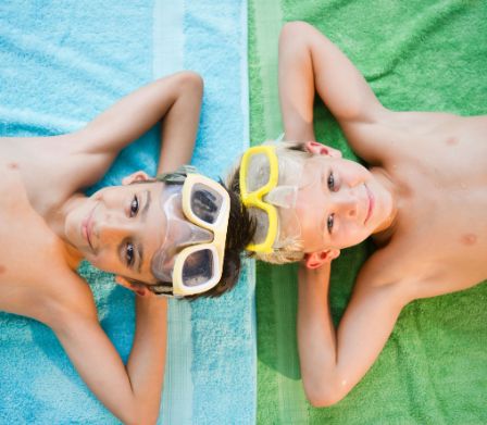 Zwei Jungs liegen mit Schwimmbrille auf einem Badetuch