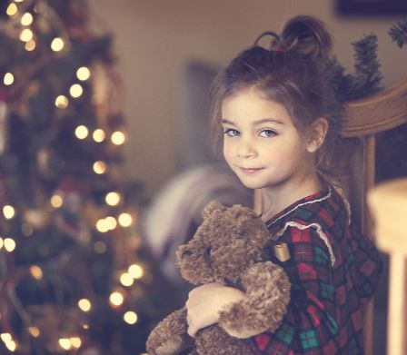 Mädchen mit Teddybär vor dem Weihnachtsbaum