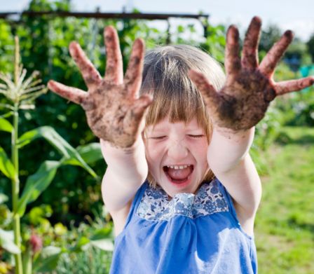 Bambina in un giardino tende in avanti le manine sporche
