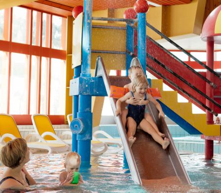 Due bambini su uno scivolo colorato in una piscina coperta 