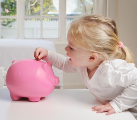 Mädchen wirft Münze in ein rosa Sparschwein