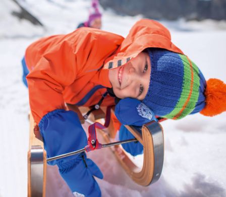 Garçon en veste de ski orange, allongé sur une luge