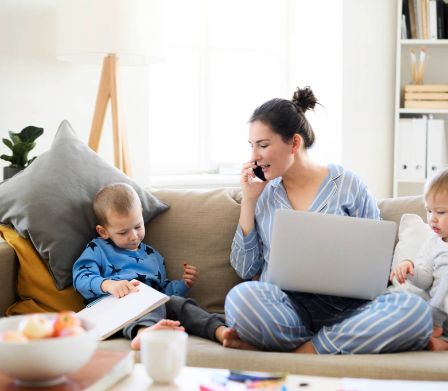 Una mamma siede con il laptop e i suoi due bambini sul divano