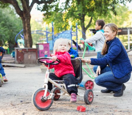Mutter und Kind auf Dreirad auf einem Spielplatz