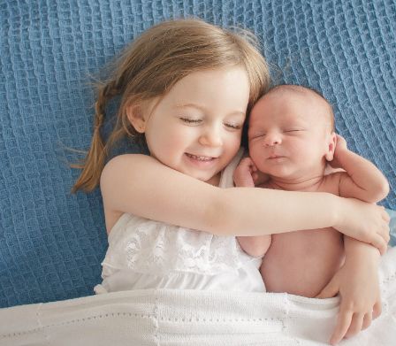 Kleines Mädchen hält lächelnd ein Baby im Arm