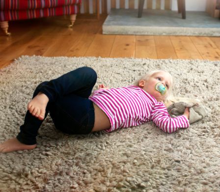 Kind liegt mit Nuggi auf einem Teppich