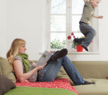 Kind springt wild auf der Couch neben der lesenden Mutter