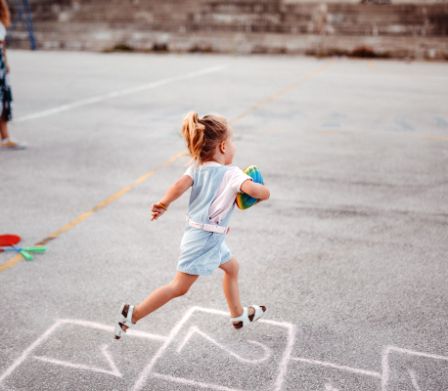Kind rennt über den Schulhof mit einem Ball