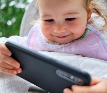 Eines kleines Kind hält freudig ein Smartphone in der Hand