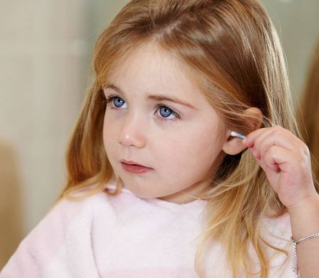 Una bambina si pulisce l'orecchio con un bastoncino ovattato