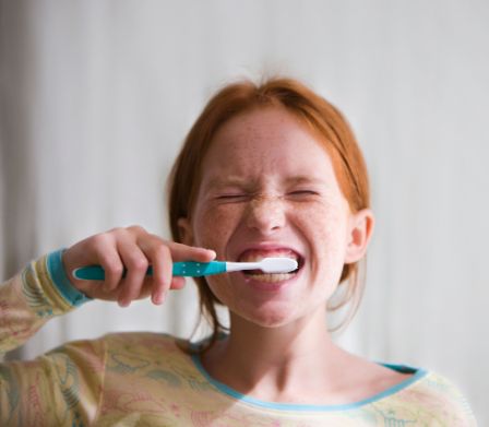 Una bambina dai capelli rossi si lava i denti