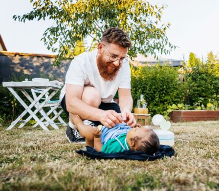 Un père change son bébé dans l’herbe
