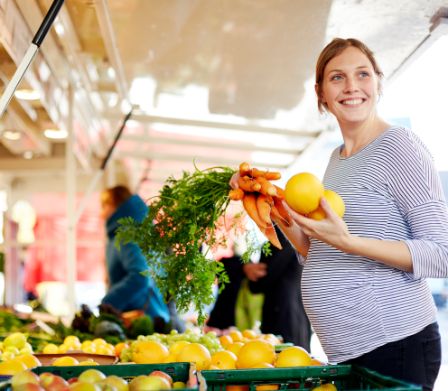 Donna incinta sorridente al supermercato con verdure in mano