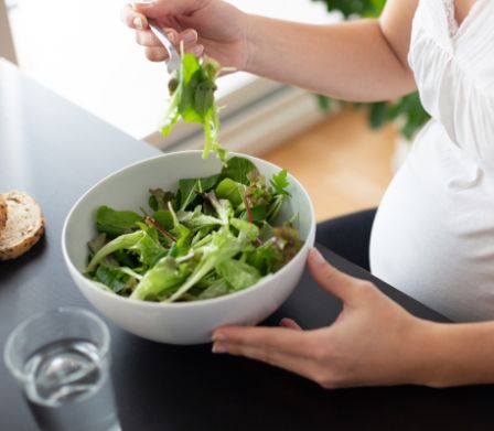 Schwangere sitzt an einem Tisch und isst einen Salat
