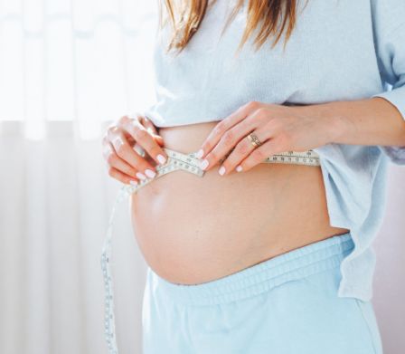Schwangere misst mit einem Massband ihren Babybauch