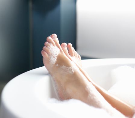 Les pieds d’une femme recouverts de mousse sur le bord de la baignoire