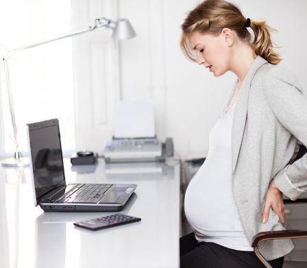Femme enceinte assise à un bureau et se tenant le dos