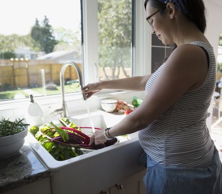 Femme enceinte en train de laver des légumes dans la cuisine