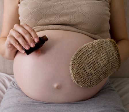 Schwangere pflegt ihren Babybauch mit Sisalhandschuh und Öl