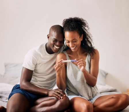 Junges Paar schaut lächelnd auf einen Schwangerschaftstest