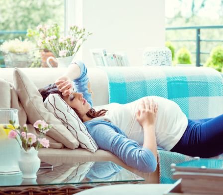 Une femme enceinte allongée sur le canapé se tient le front et le dos
