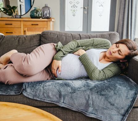 Schwangere Frau liegt auf dem Sofa und hält sich den Bauch 
