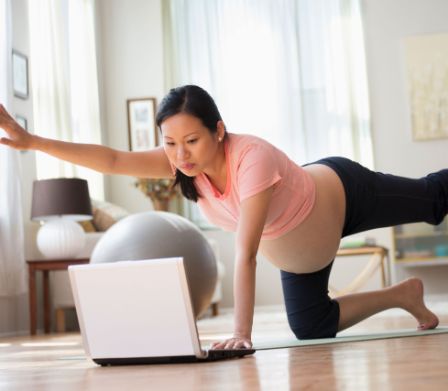 Schwangere macht am Boden Übungen vor dem Laptop
