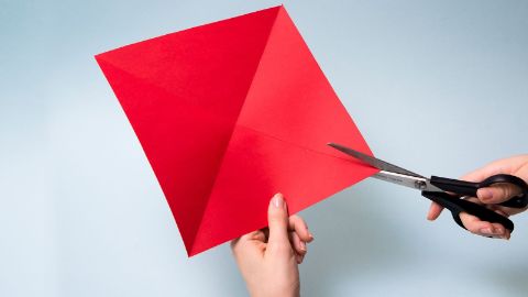 Découper un grand carré dans la feuille de papier rouge, le plier en triangle et l’inciser.