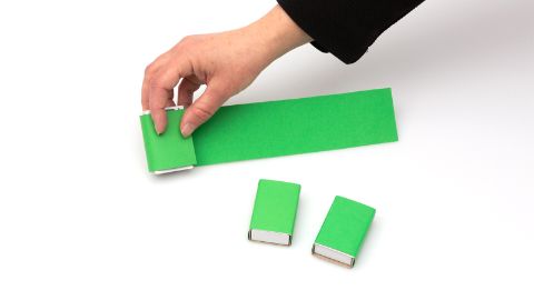 Drei Zündholzschachteln werden mit einem grünen Papier beklebt