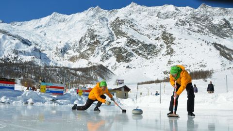 Due uomini giocano a curling su una pista di ghiaccio naturale