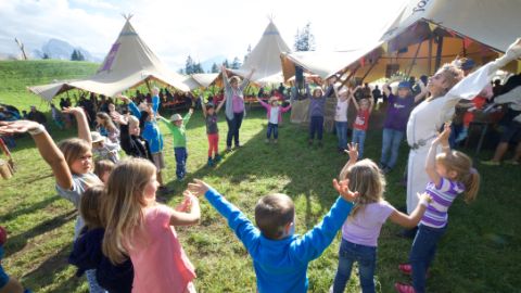 Kinder und Animateure vor Zelten stehen im Kreis und heben die Arme Kinder und Animateure vor Zelten stehen im Kreis und heben die Arme