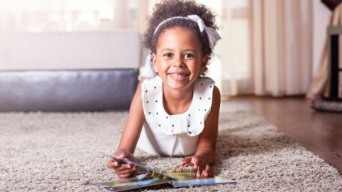 Un bambino legge un libro sdraiato sul tappeto